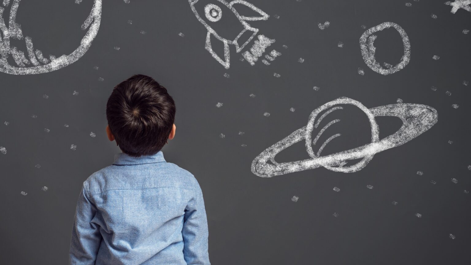 Boy with autism spectrum disorder (ASD) looking intently at a chalk drawing of space on the ground. The image captures wonder, focus, and a deep connection to special interests often seen in autistic children.